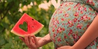 A slice of watermelon in the hands of a pregnant woman